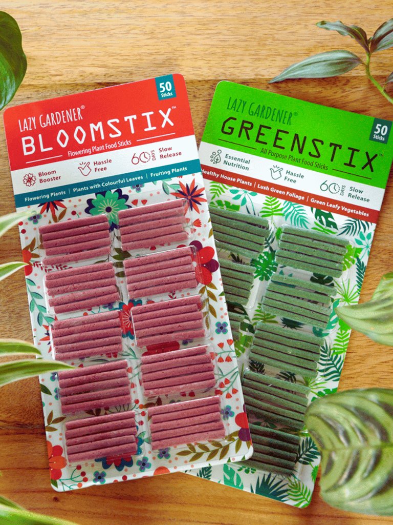 Packaging of Lazy Gardener Fertilizer Food Sticks, with one pack labeled 'Greenstix' and the other 'Bloomstix'. Both packs are decorated with colorful floral designs and product information.